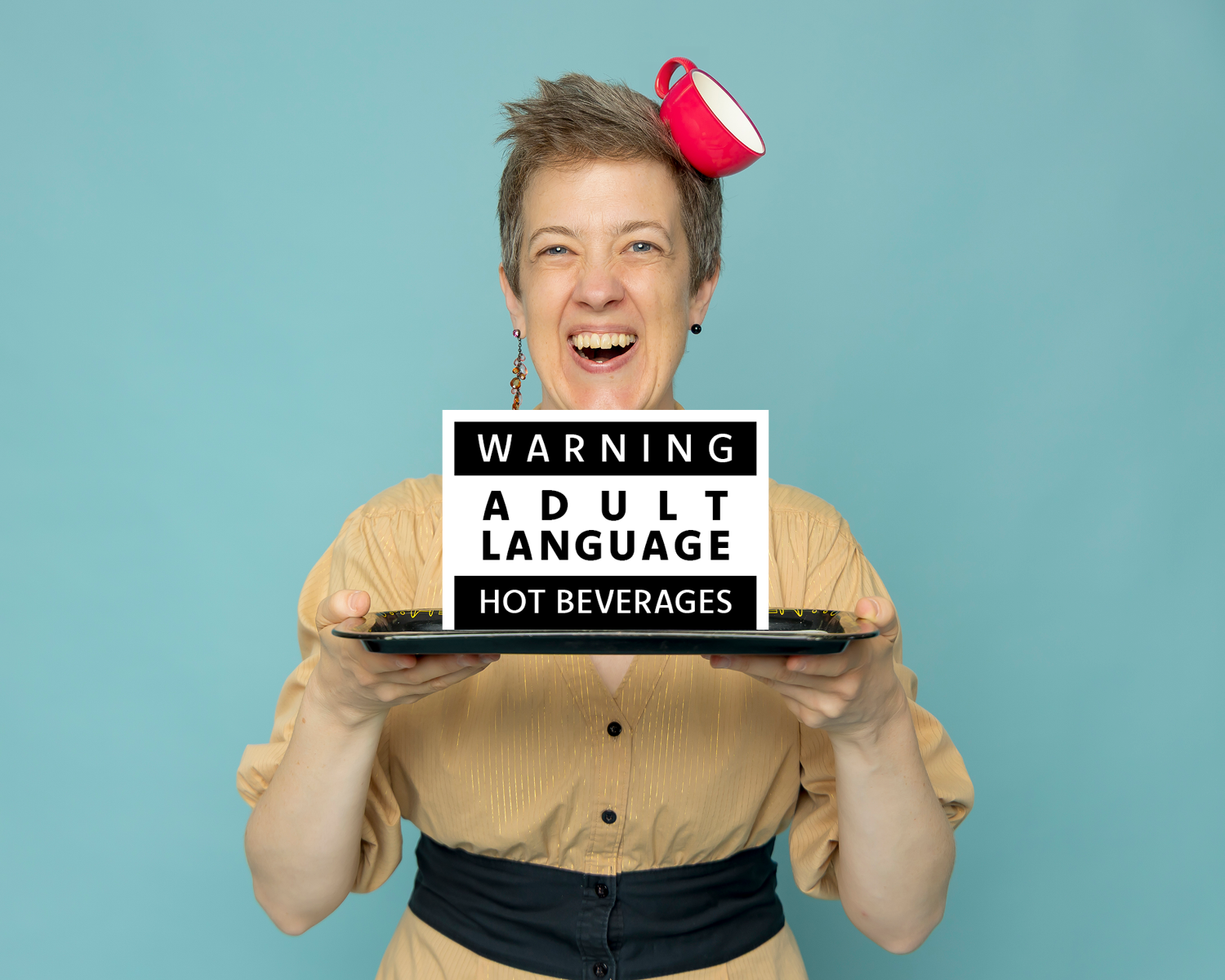 Erika MacDonald laughing as she holds a tray with a warning sign reading Adult Language, Hot Beverages