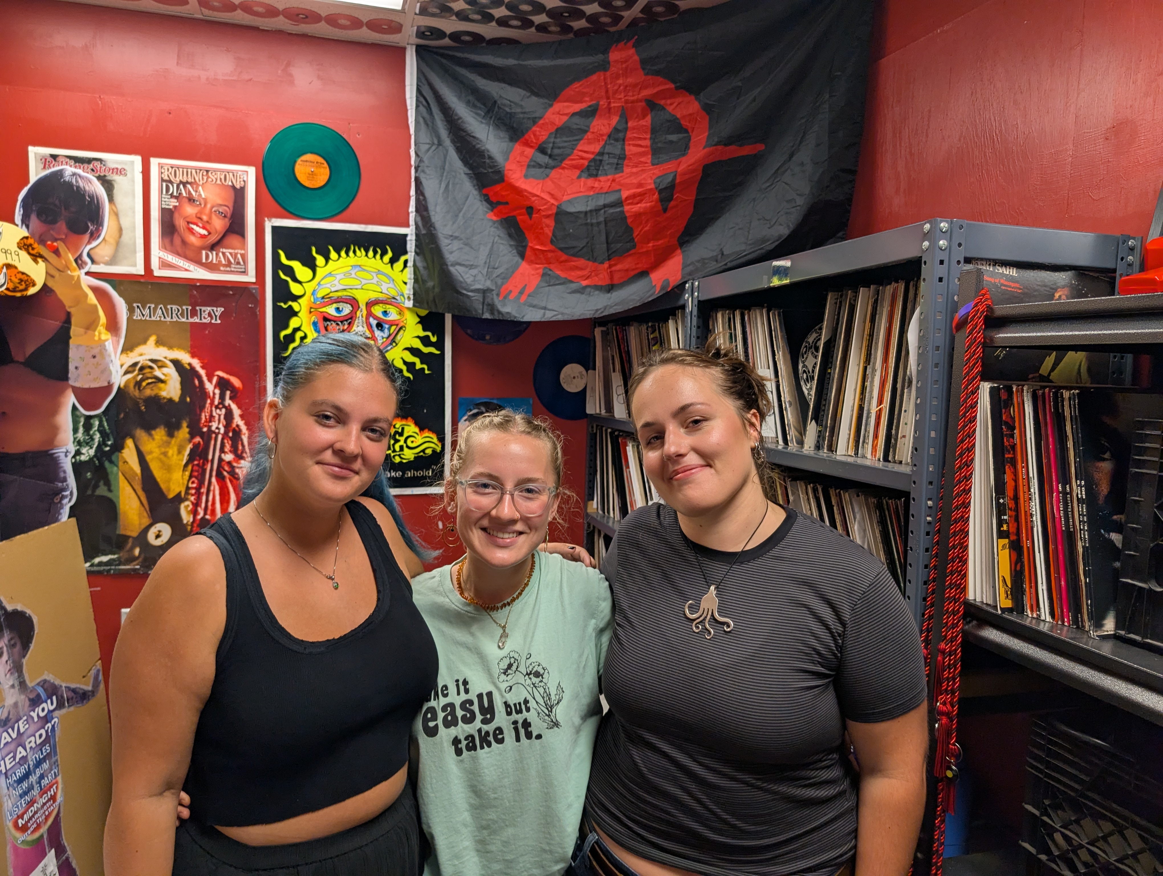 Three student DJs smiling in the WECX studio in front of shelves of vinyl records