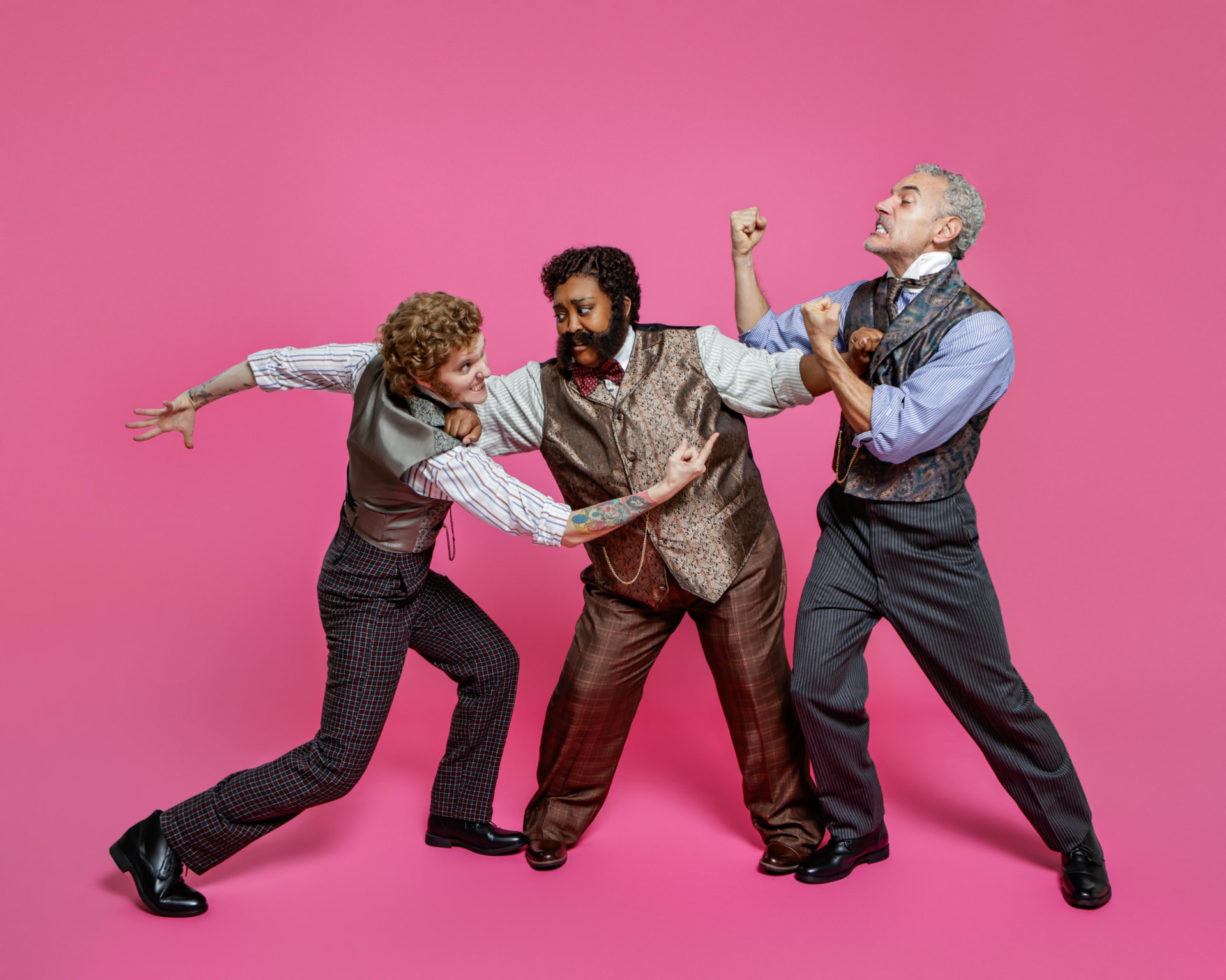 Three Ahoy-Hoy cast members in period costume wrestle in a comic three-way fight against a pink backdrop.