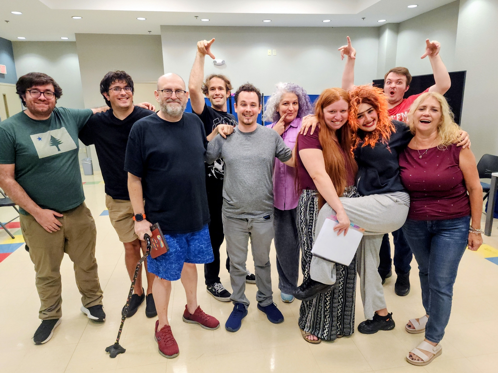 The cast of Dracula: A Comedy of Terrors, about a dozen people of many ages, pose and mug for the camera in a community center room.