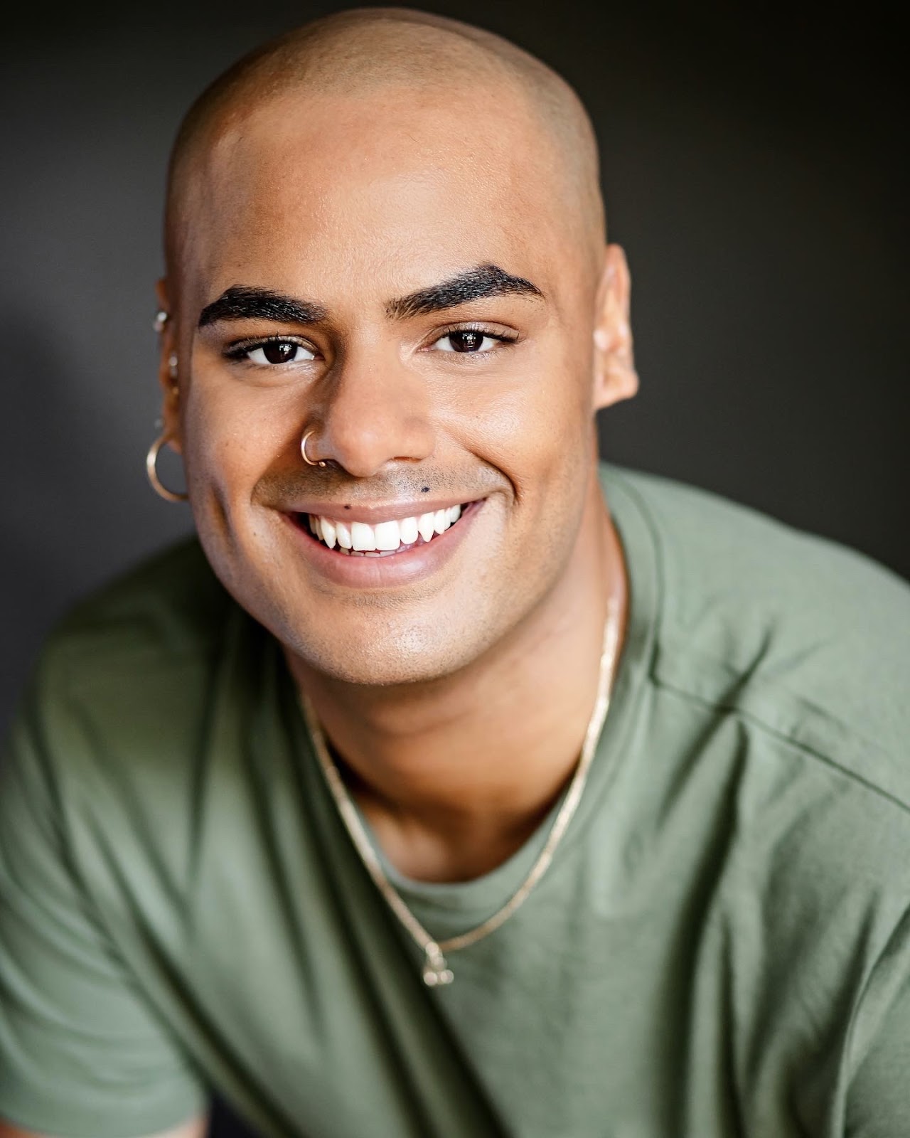 Headshot of Auston Henderson, who plays George Washington in the North American tour of Hamilton, smiling in a green t-shirt against a dark background.