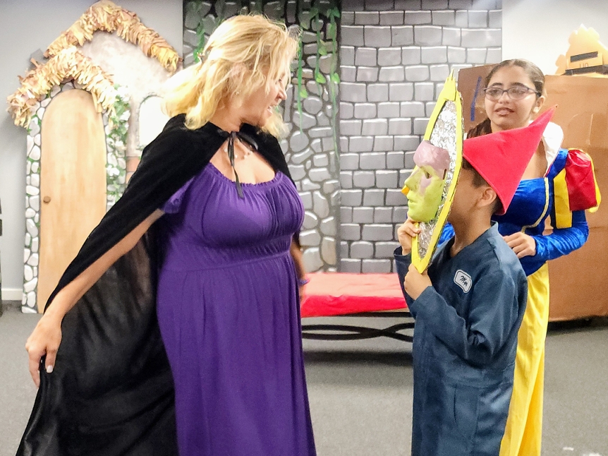 An Evil Queen faces off with a young Snow White holding a mirror.