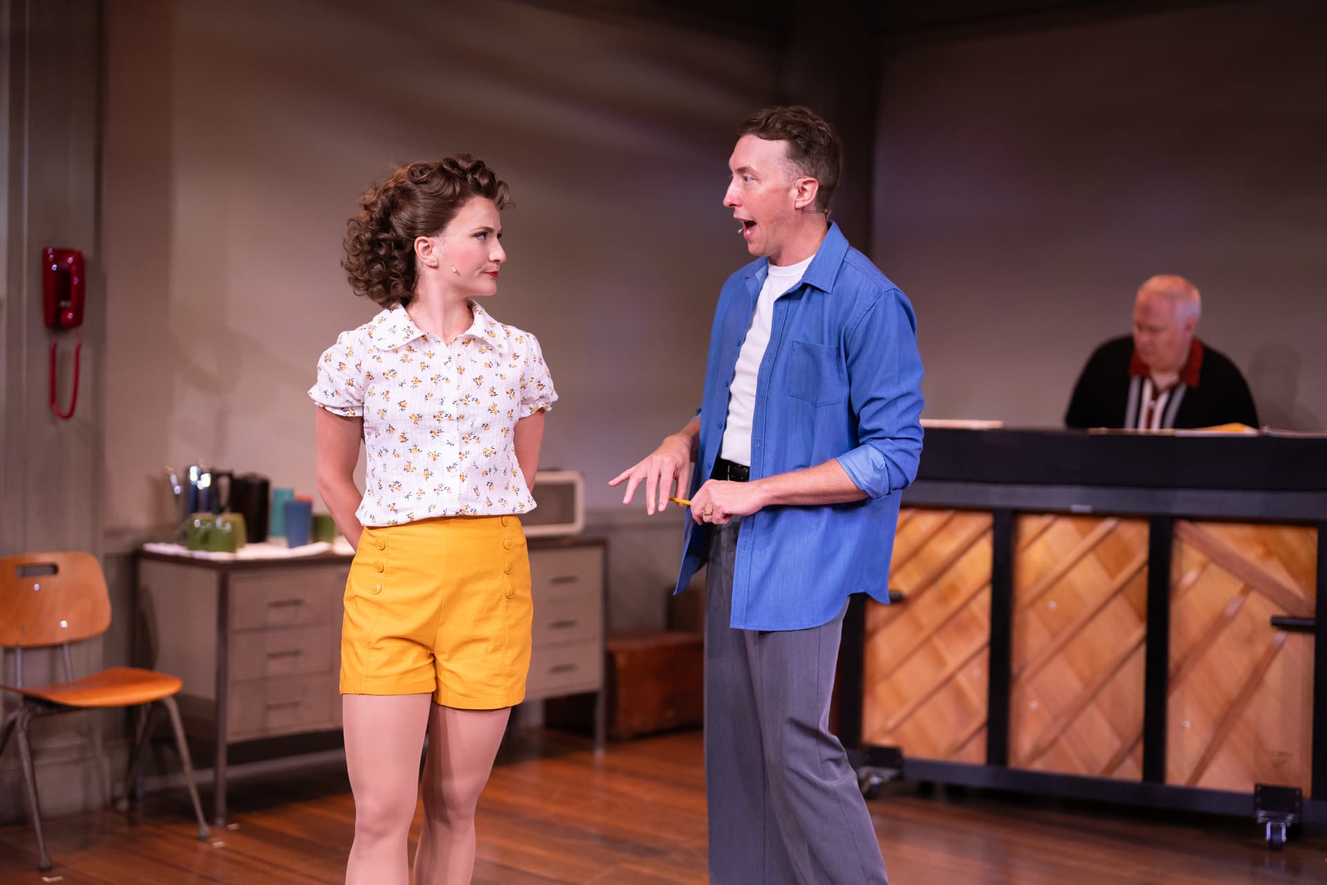 Two actors in 1950s costume face each other mid-scene in a rehearsal room set
